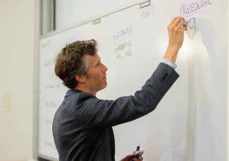 Tom Dannenbaum writes on a whiteboard in a classroom on Fletcher's campus. 