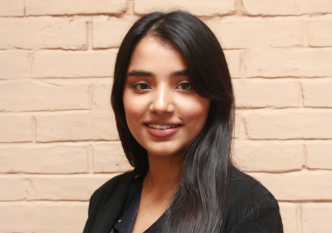 Manashi Pandit smiles in a close-up in front of a peach, brick background.