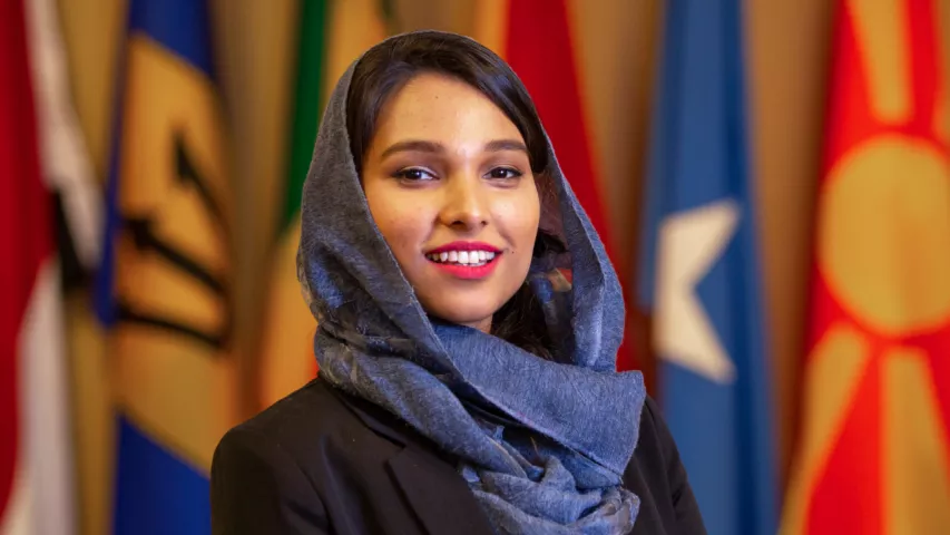 Faiqa Naseem smiles in front of a background of flags.