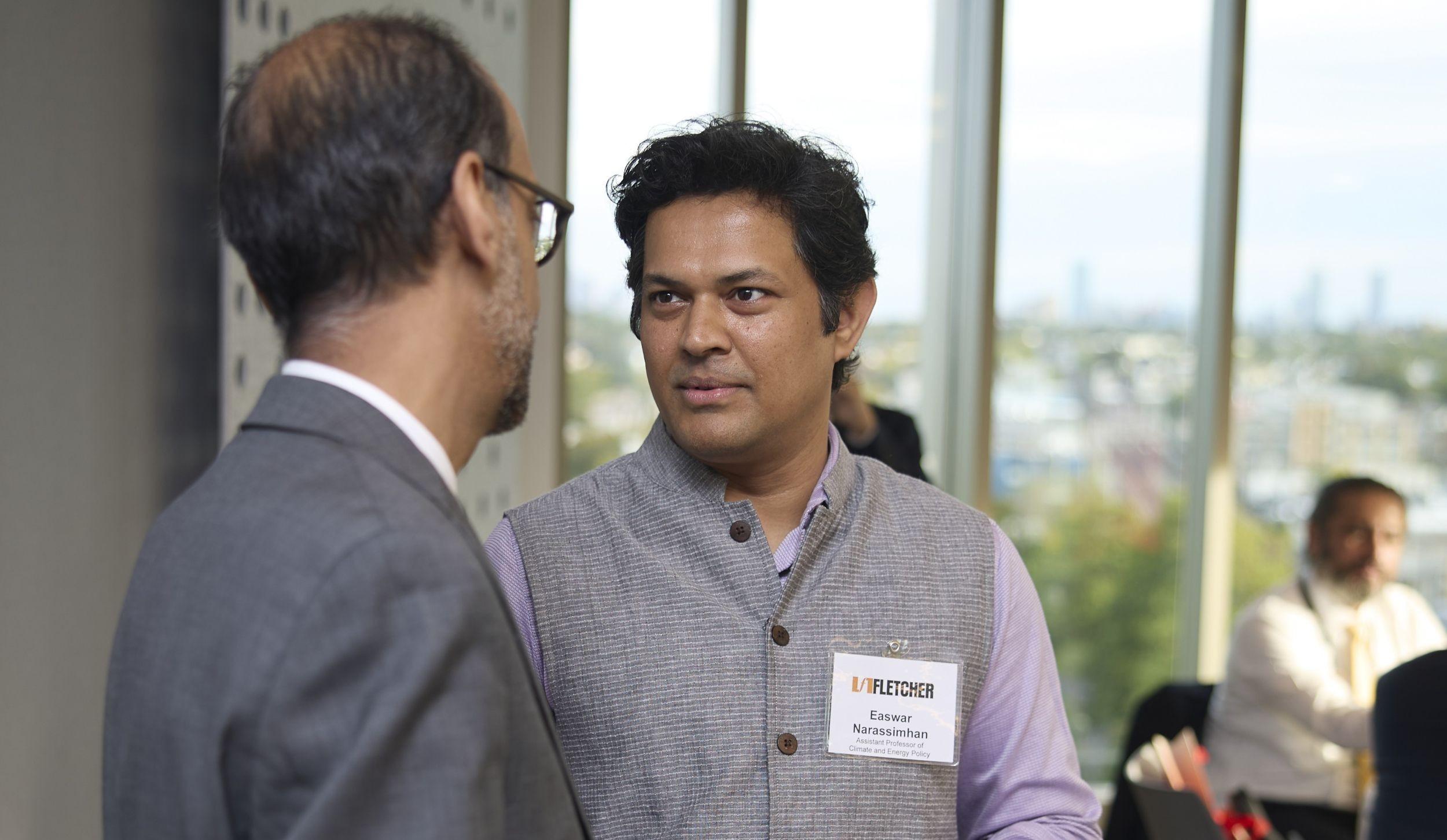 Easwaran Narassimhan speaks with Alnoor Ebrahim inside of a room with sunny windows in the background.
