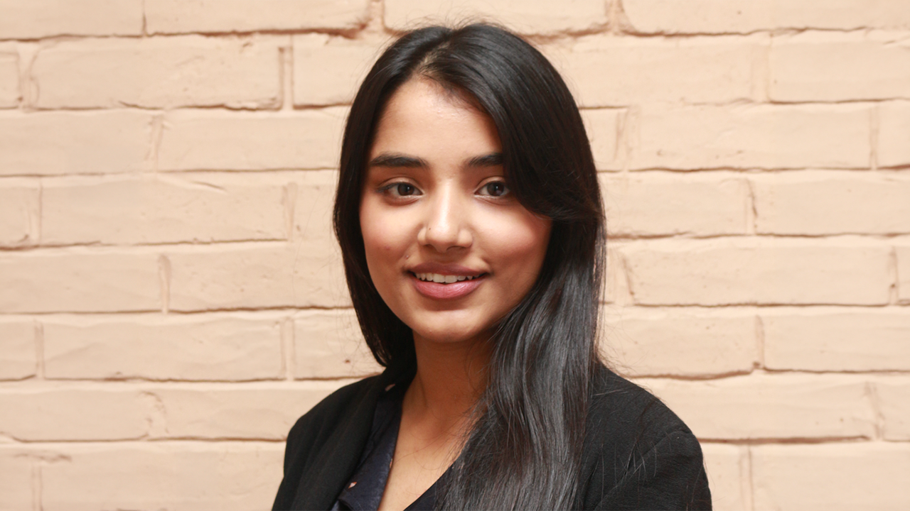 Manashi Pandit smiles in a close-up in front of a peach, brick background.