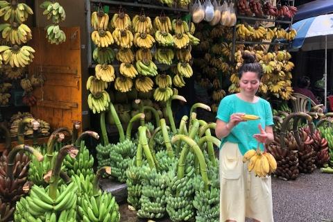 Hattie Brown holds a bunch of bananas in front of a banana stand. 