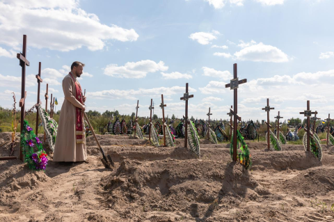 A man stands in a graveyard in Bucha, Ukraine, among crosses and freshly dug graves.