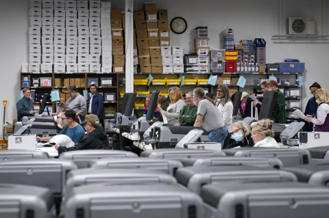 People standing around large numbers of voting machines. A Tufts cybersecurity expert says one of the best ways to secure electronic voting systems is to use election equipment that creates a paper record of every vote cast