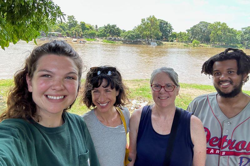 Four people smile for the camera in front of a river in the background. 