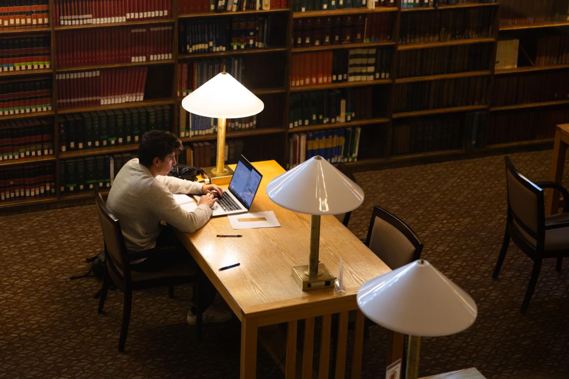 Student sits at a desk in a library with the table lamp on