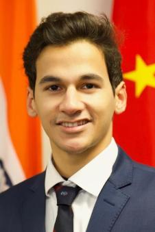 A headshot of Armaan Mathur in front of flags in the background