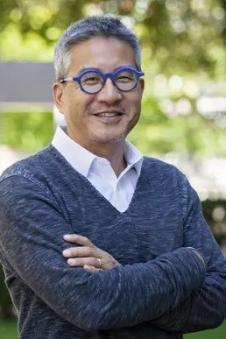 A headshot of Joseph Wong in front of a green, outdoor background