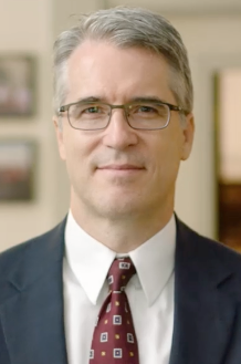 A headshot of William Grimes in front of a blurry indoor background