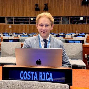 Raffael Huberli sits in front of a laptop at a placard reading, "Costa Rica." 