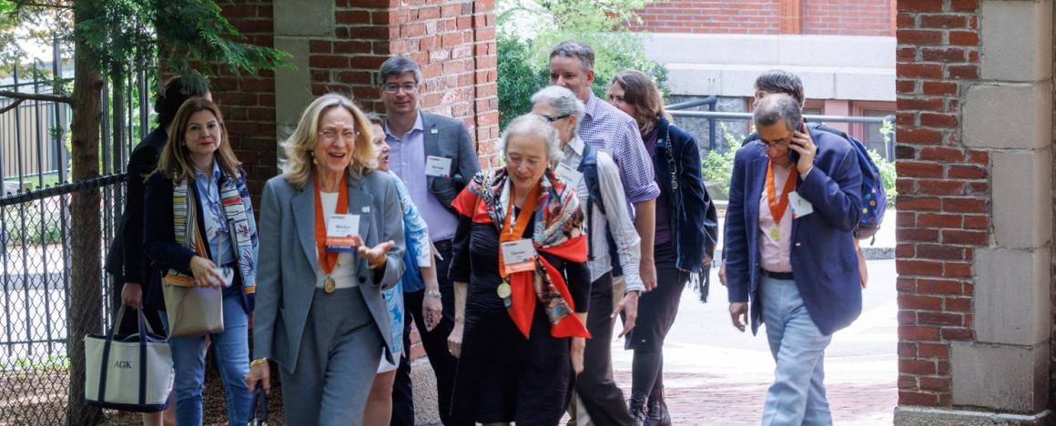 Several people with name tags walk outside on a path through an arch, talking