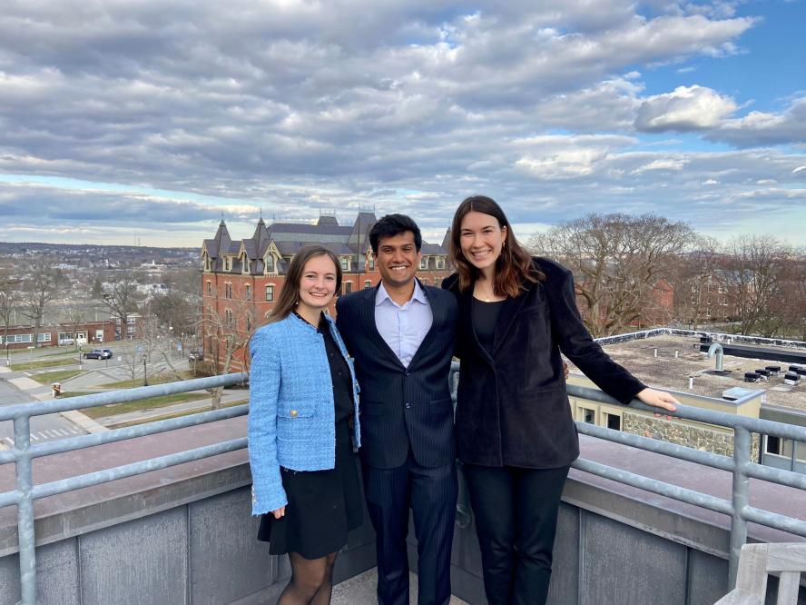 Fiona Negron, wearing a light blue jacket; Gaurav Redhal, wearing a blue suit and Sophia Warner, wearing a black suit on a balcony of the Cabot building
