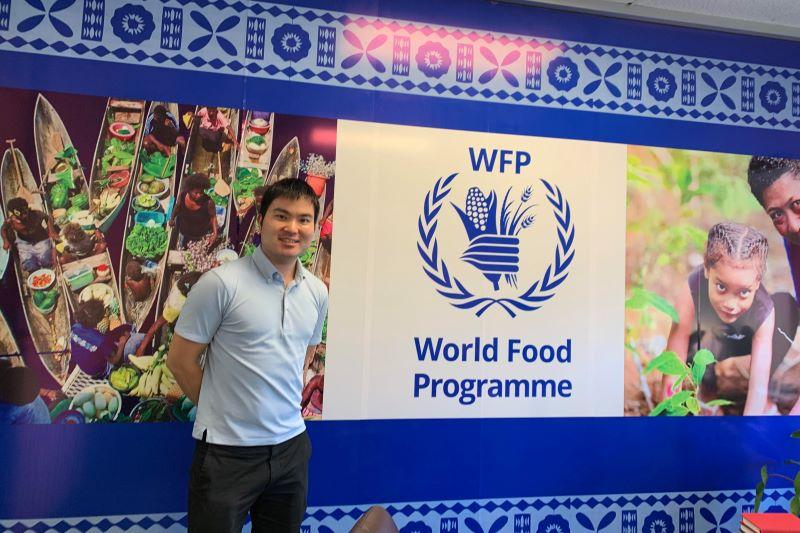 Daiki Tajima poses in front of a banner for the United Nations World Food Programme