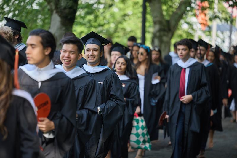Class of 2023 graduates assemble in a line outside on campus