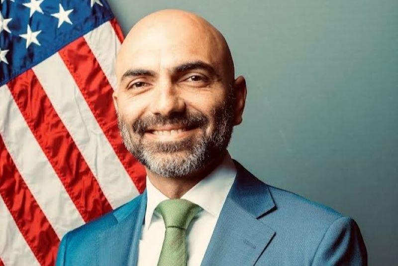 A close-up headshot of Mustafa Popal in front of the American flag.