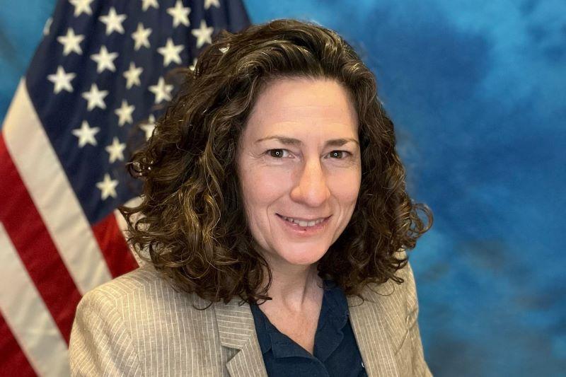 A headshot of Robin Brooks in front of the American flag and a blue background.