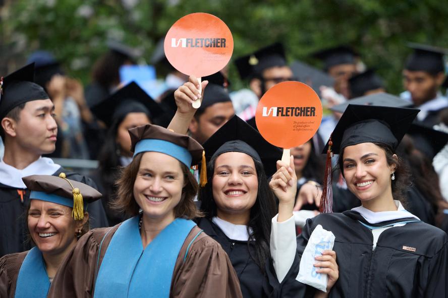 Fletcher graduates smiling and holding up round, orange paper paddles that say Fletcher