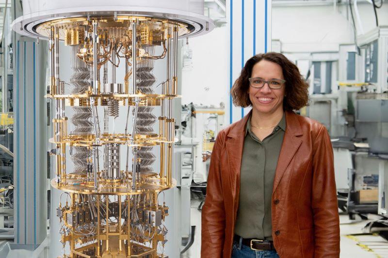 Mandy Birch smiles, standing beside a quantum computer.