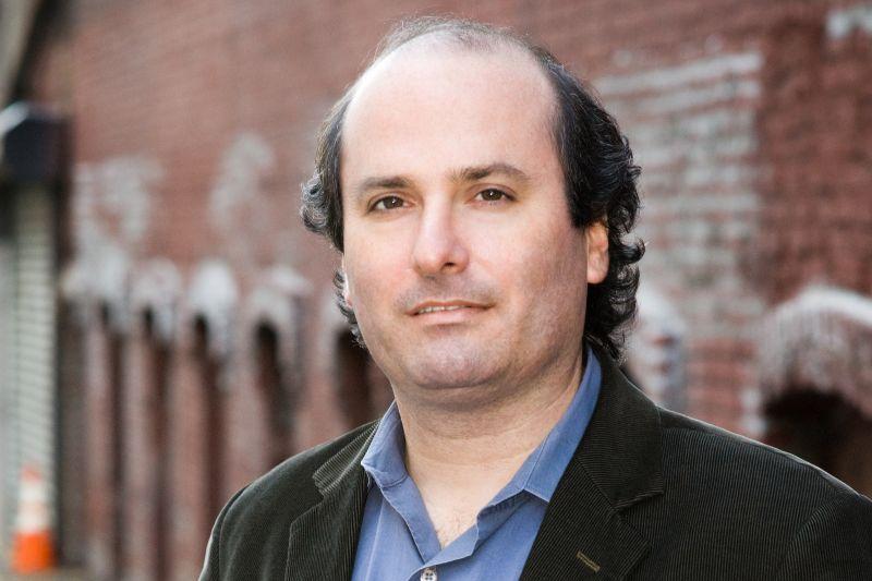A headshot of David Grann in front of a brick wall.