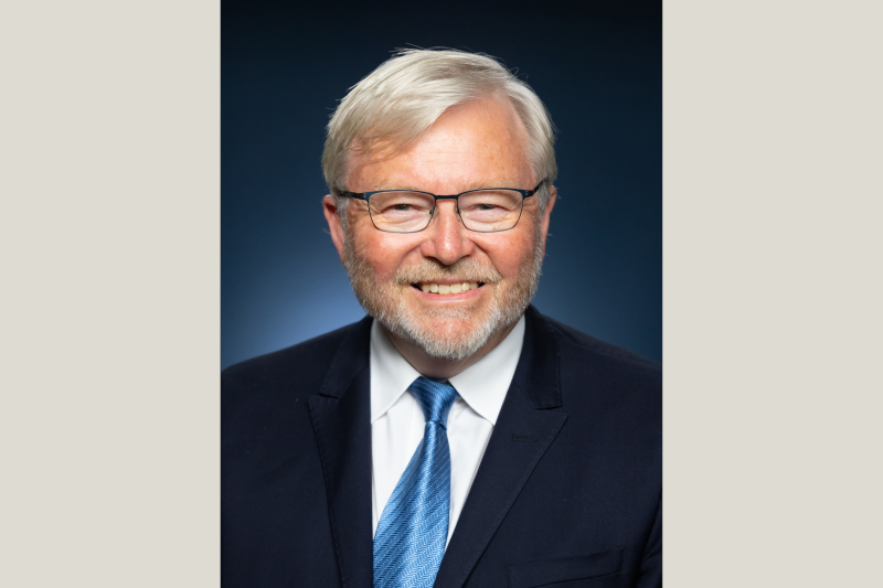 A headshot of He the Honorable Dr. Kevin Rudd smiling in front of a blue background.