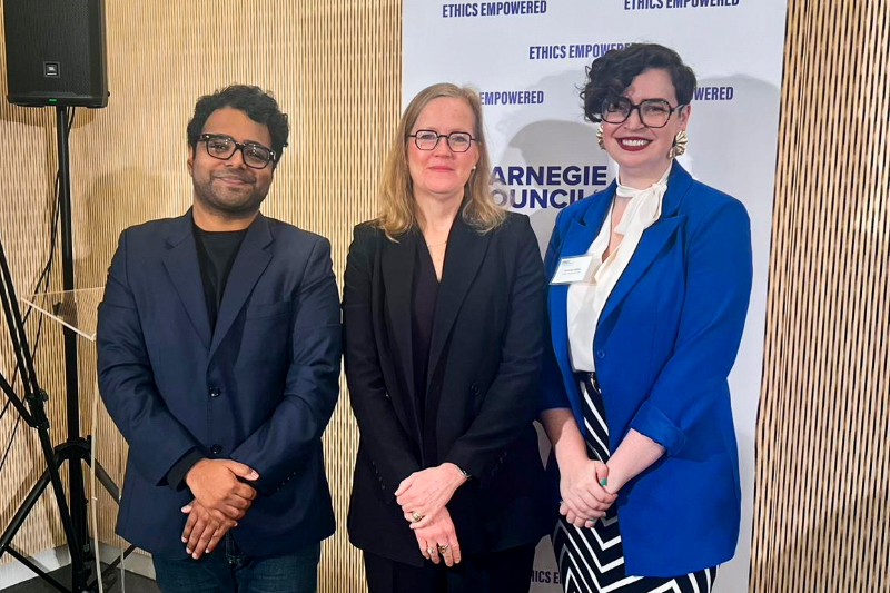 Vishal Manve, Monica Toft, and Samantha Hubner pose for a picture in front of a Carnegie Council banner.