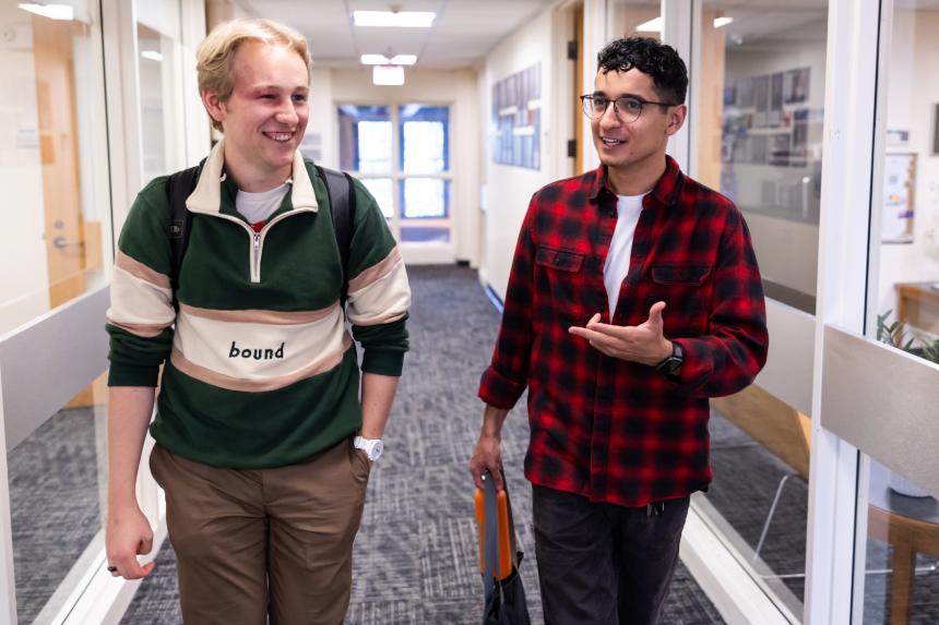 Two students walk down a hallway, talking and laughing