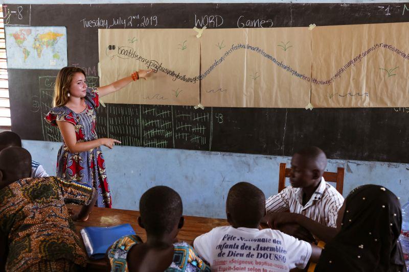 Emma Bixler stands in front of a chalkboard, teaching a class of students in Benin.