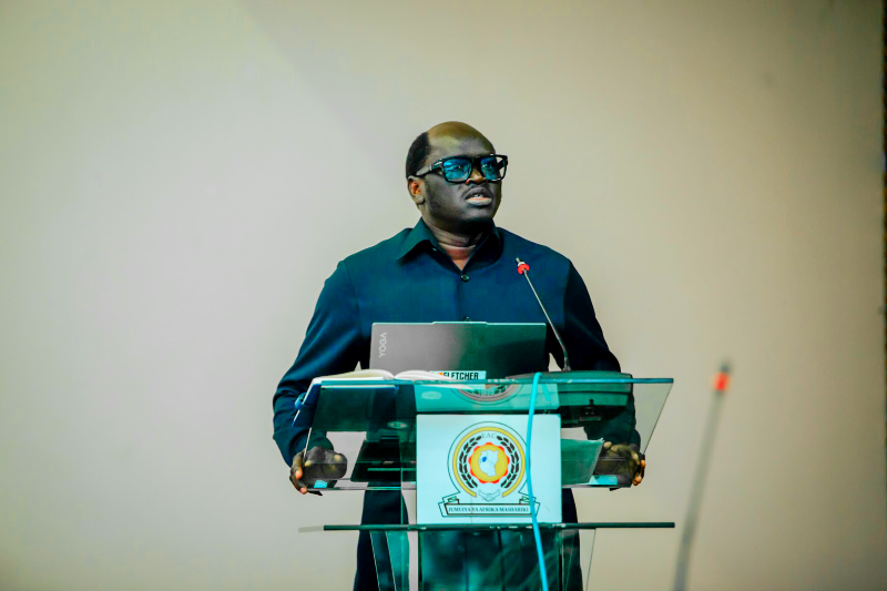 Nicodemus Ajak Bior stands at a podium with an open laptop, giving a speech.