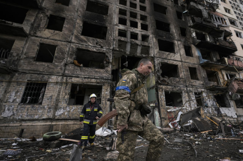 Ukrainian soldier walking past a bombed-out building.