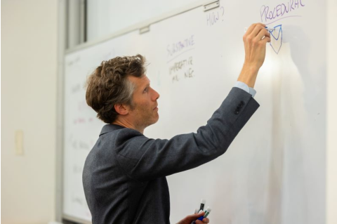 Tom Dannenbaum writes on a whiteboard in a classroom on Fletcher's campus. 