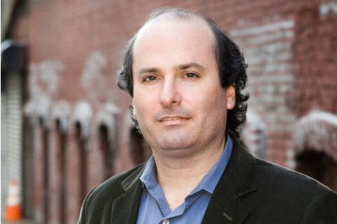A headshot of David Grann in front of a brick wall. 