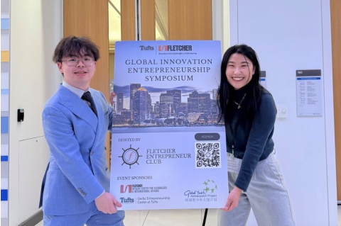 Sophie Hu and Jojo Zhou hold the symposium poster, smiling.