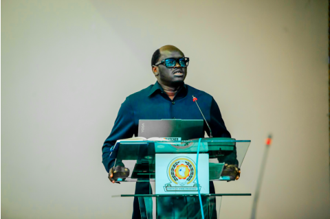 Nicodemus Ajak Bior stands at a podium with an open laptop, giving a speech.