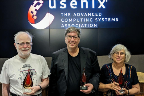 Two men and one woman hold awards in the shape of flames in front of a sign for USENIX: The Advanced Computing Systems Association. Susan Landau receives prestigious USENIX Lifetime Achievement Award