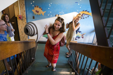 Two students carry a rolled carpet up a set of stairs in a dormitory