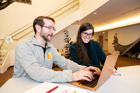 A man and woman seating at a table, the man typing on a laptop. The new Tufts  Cybersecurity Clinic pairs computer science students with small organizations to ward off intruders