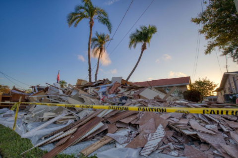 Caution tape stretches in front of debris near a Florida home damaged by a hurricane